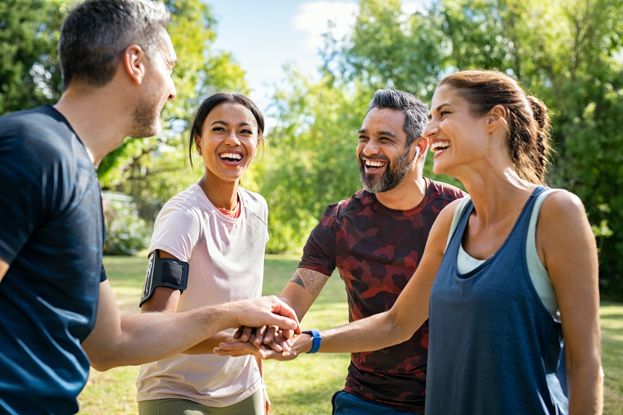 Group of active mature friends in park stacking hands after workout
